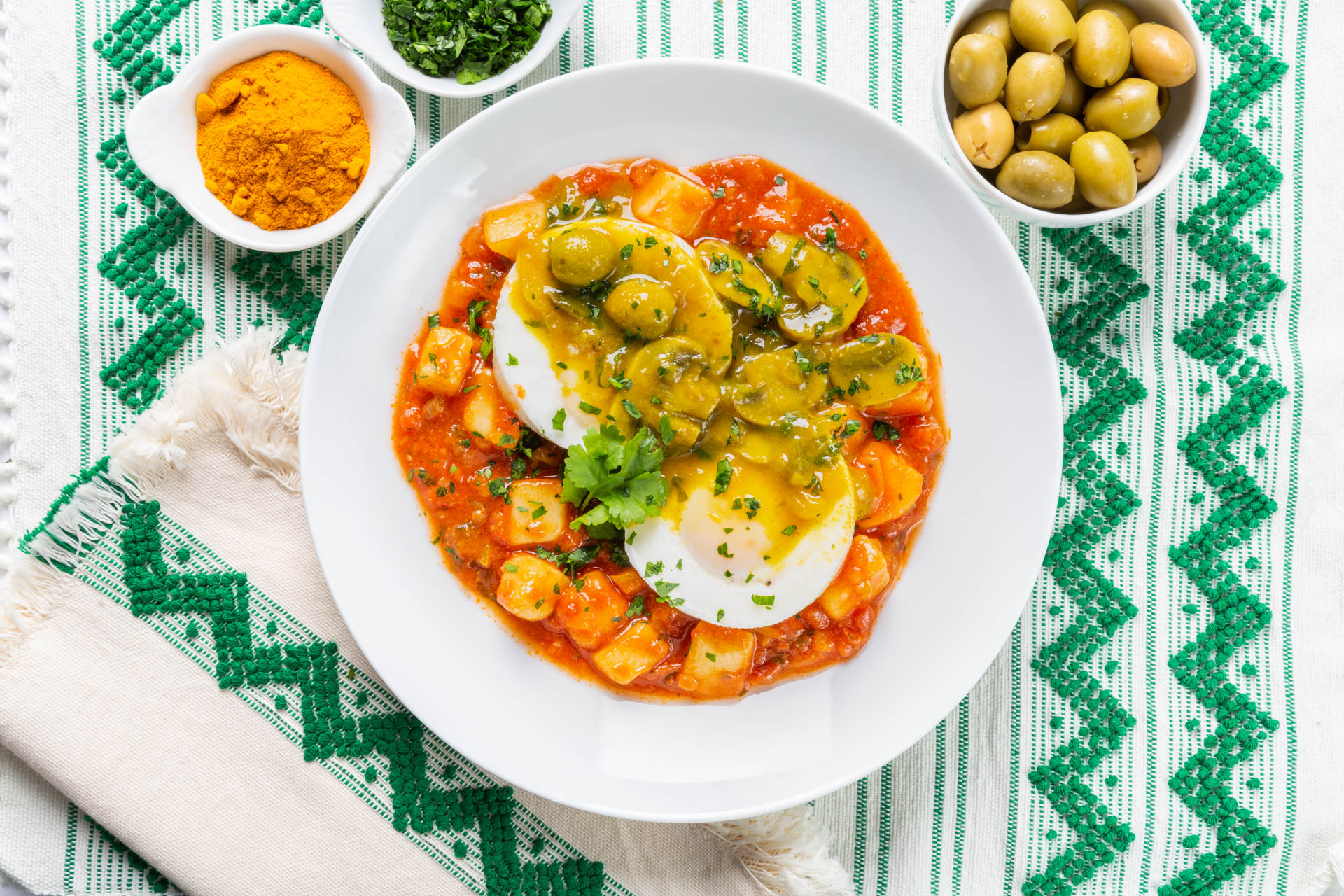 A bowl of shakshuka on a green and white tablecloth 