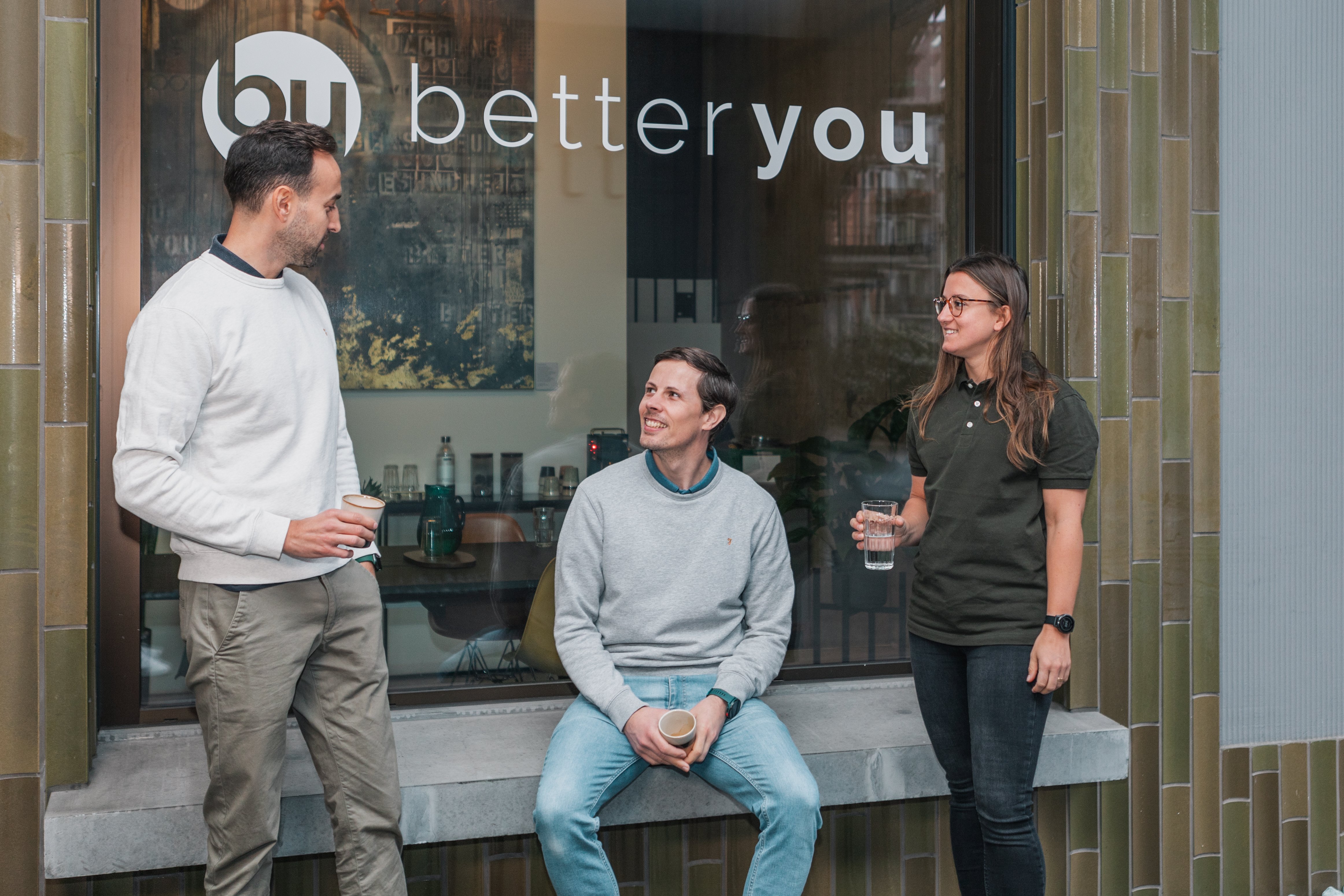 three people in front of a shop window, one of them seated